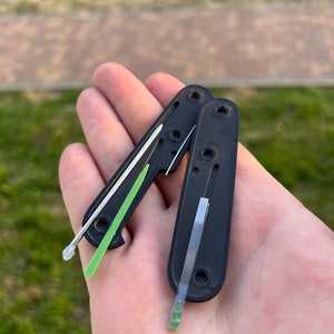 May include: Two black pocket knives with green and silver blades. The blades are partially extended.