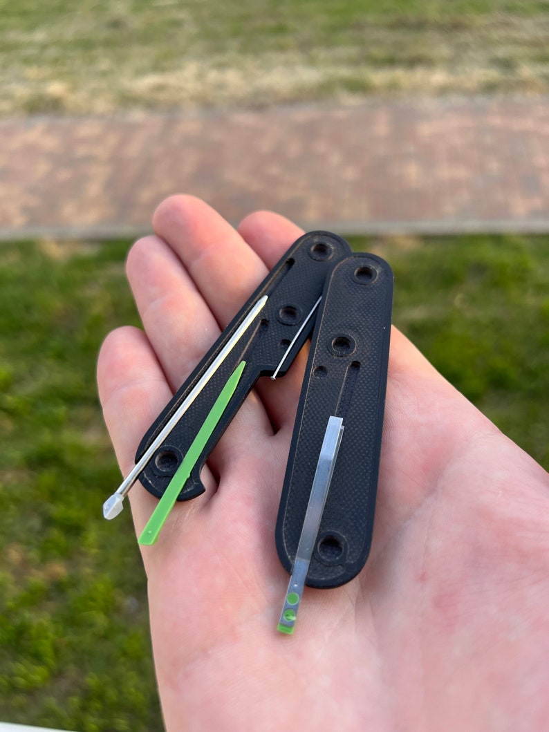 May include: Two black pocket knives with green and silver blades. The blades are partially extended.