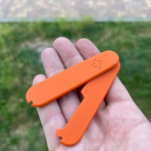 May include: Two orange plastic tools with a textured surface. The tools are folded together and have a plus sign on one side.
