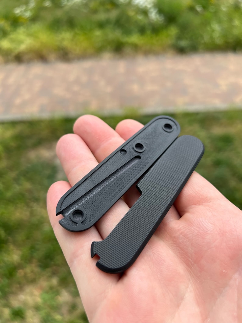 May include: Two black plastic scales for a pocket knife. The scales have a textured surface and a hole for a screw.