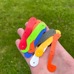 Peut inclure: Un ensemble de huit porte-clés en plastique de couleurs vives, de formes variées, dont un oiseau, un poisson et un cœur. Les porte-clés sont disposés dans une main, le porte-clés rouge en haut et le porte-clés orange en bas.