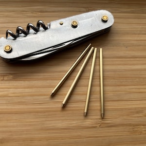 Può includere: Un multiutensile argentato con un cavatappi e un set di quattro strumenti in metallo dorato.