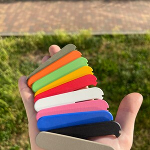 May include: A set of ten different coloured plastic scales, stacked on top of each other. The colours are grey, black, blue, pink, white, red, yellow, green, orange, and brown.