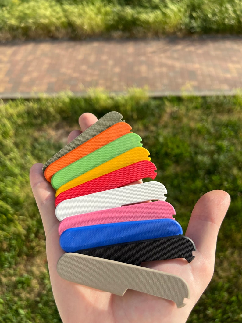 May include: A set of ten different coloured plastic scales, stacked on top of each other. The colours are grey, black, blue, pink, white, red, yellow, green, orange, and brown.