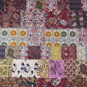 Könnte beinhalten: Ein Patchwork-Textil mit verschiedenen gemusterten Stoffquadraten. Das Design umfasst Paisley-, Blumen- und geometrische Muster in Burgunder-, Blau-, Gold- und Lilatönen. Das Textil hat eine Cordstruktur.
