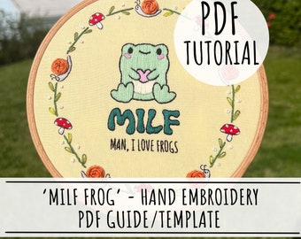 Peut inclure: Un motif de broderie à la main pour un projet d'art de cerceau représentant une grenouille verte tenant un cœur avec le texte "MILF" et les mots "MAN, I LOVE FROGS" en dessous. Le motif est entouré d'une couronne de feuilles, de champignons et d'escargots.
