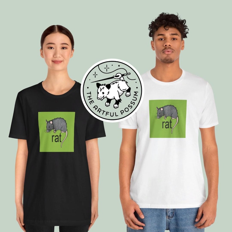 Puede incluir: Dos personas con camisetas negras y blancas con un gr&aacute;fico cuadrado verde que muestra una rata y la palabra "rat". La camiseta negra tiene una pegatina circular blanca con una ilustraci&oacute;n de zarig&uuml;eya y el texto "The Artful Possum".