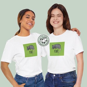 Puede incluir: Dos personas con camisetas blancas con un gr&aacute;fico cuadrado verde que muestra una rata y el texto "rat". El gr&aacute;fico es de "The Artful Possum".