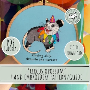May include: Hand embroidery pattern featuring a gray opossum wearing a colorful jester's collar and party hat. The opossum is embroidered on a light blue fabric, with the text "staying silly despite the horrors". Includes "PDF Tutorial" and "Digital Download" labels.
