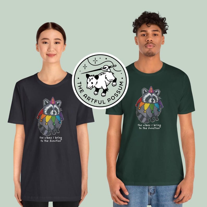 May include: Two people wearing black and green t-shirts with a raccoon wearing a jester hat and rainbow colors. The text on the shirts reads "the vibes I bring to the function". A logo for "The Artful Possum" is in the background.