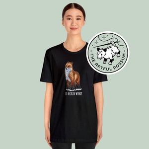 May include: Black t-shirt with a red fox illustration and the text "It heckin wimdy". The t-shirt also features a white circle with a black and white possum illustration and the text "The Artful Possum".