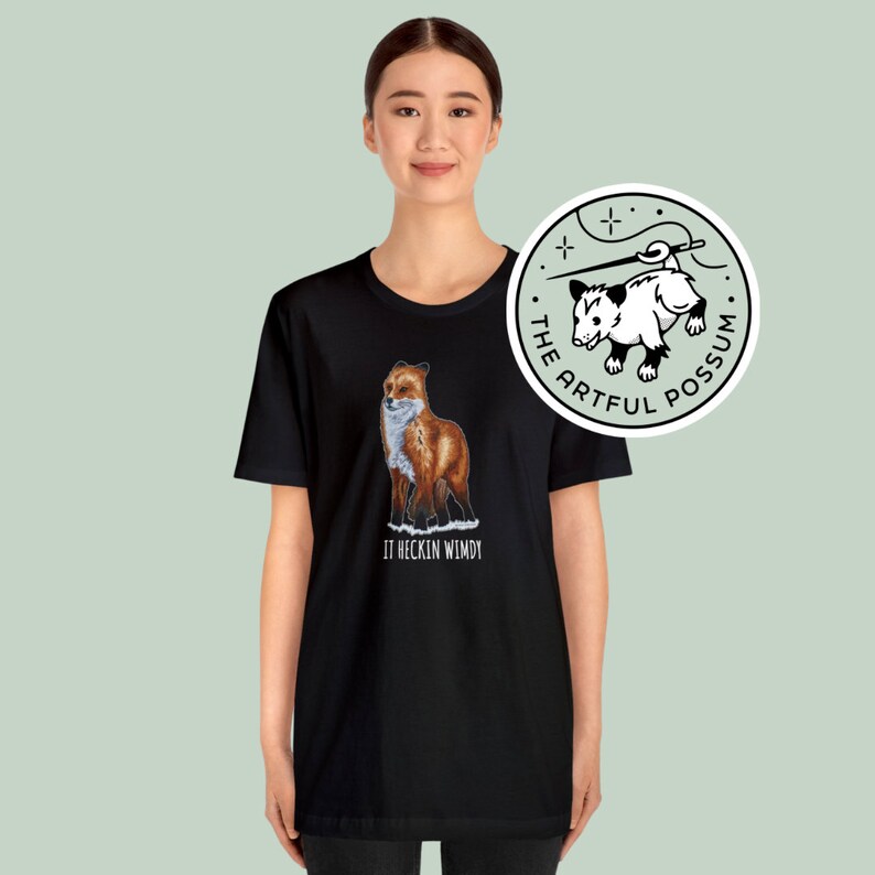 May include: Black t-shirt with a red fox illustration and the text "It heckin wimdy". The t-shirt also features a white circle with a black and white possum illustration and the text "The Artful Possum".