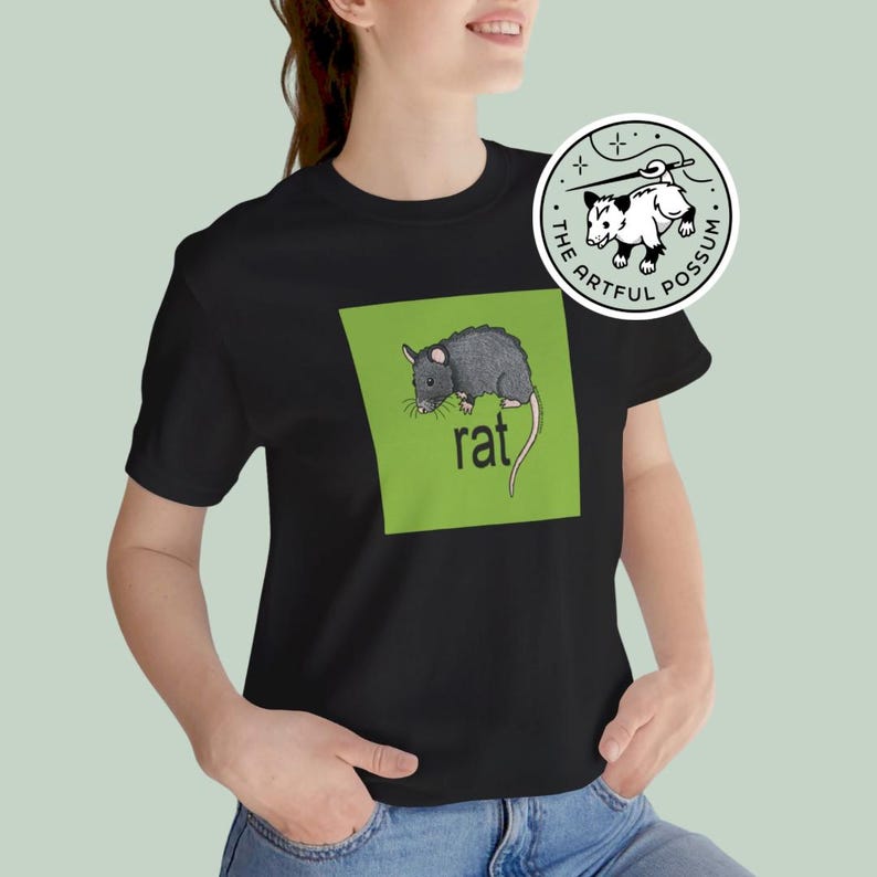 Puede incluir: Una camiseta negra con un cuadrado verde que presenta una ilustraci&oacute;n de rata negra y la palabra "rat" en texto blanco. La camiseta tiene un logotipo blanco con una ilustraci&oacute;n de zarig&uuml;eya negra y el texto "The Artful Possum".