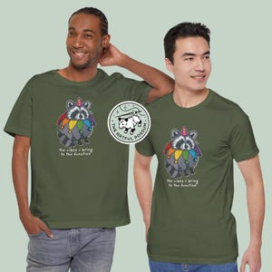 May include: Two men wearing olive green t-shirts with a graphic of a raccoon wearing a jester's hat and rainbow-colored collar. The text on the shirt reads "the vibes I bring to the function". The graphic also includes a small logo that reads "The Artful Possum".