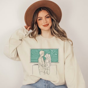 May include: A light beige sweatshirt with a green chalkboard graphic featuring a couple holding hands. The chalkboard has handwritten text that reads "I love you more than words can say" and "We are a match made in heaven".