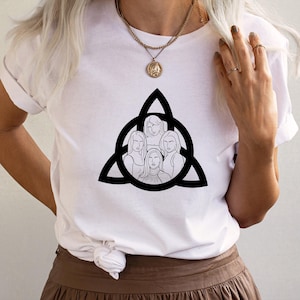 Pode incluir: Camiseta branca com um gráfico preto e branco de cinco mulheres em um círculo com um design de nó celta.