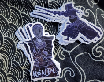May include: A stack of white stickers with a black outline of a person wearing a kendo uniform and holding a sword. The sticker says "KENDO" in white lettering.