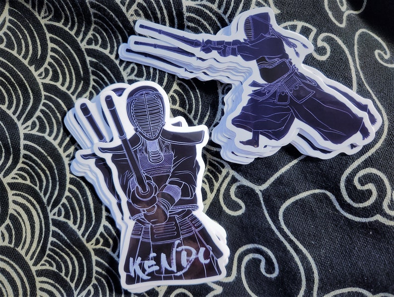 May include: A stack of white stickers with a black outline of a person wearing a kendo uniform and holding a sword. The sticker says "KENDO" in white lettering.