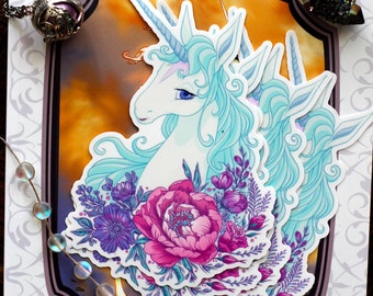 May include: A stack of four stickers featuring a white unicorn with a blue mane and tail, surrounded by pink and purple flowers. The stickers are on a white background with the text "The Last Unicorn" and "Peter S. Beagle".