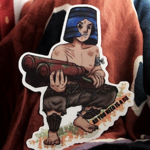Könnte beinhalten: Ein Aufkleber mit einer Comicfigur, die einen blauen Helm trägt und eine große rote und braune Waffe hält. Die Figur hockt und der Aufkleber hat den Text "All you need is a DB" aufgedruckt.