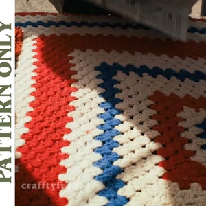 Op de afbeelding: Een close-up van een gehaakt deken met rode, witte en blauwe vierkanten. Het deken is gemaakt met een eenvoudig granny square patroon.