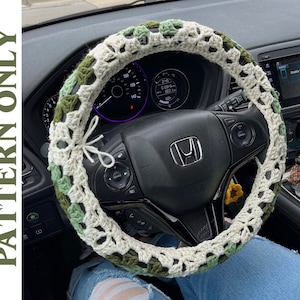 May include: A handmade crochet steering wheel cover in shades of cream, green, and olive. The cover is attached with a white string and is shown on a black steering wheel inside a car. The text "PATTERN ONLY" is visible on the left side.