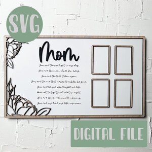 Op de afbeelding: Een wit houten bord met een zwarte inscriptie die "Moeder" luidt en een gedicht over moederschap. Het bord heeft vier rechthoekige uitsparingen voor foto's. Het bord is omgeven door een decoratieve bloemvormige rand.