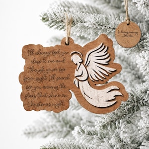 May include: A light brown wooden ornament featuring a laser-engraved angel and the text: I'll always feel you close to me and though you're far from sight, I'll search for you among the stars that shine on Christmas night. Includes a round tag.