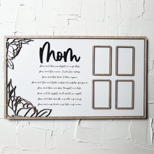 Op de afbeelding: Een wit houten bord met een zwarte uitsparing van het woord "mom" en een gedicht over moederschap. Het bord heeft vier rechthoekige ruimtes voor foto's.