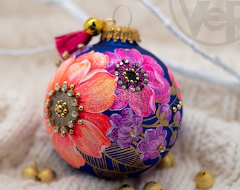 May include: A blue Christmas bauble with a hand-painted design of pink and orange flowers, gold accents, and rhinestones.