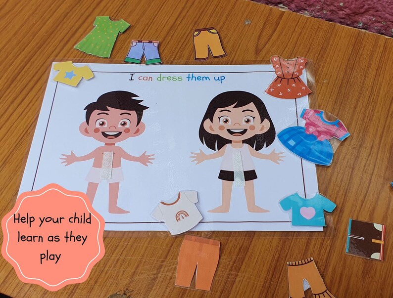 May include: A learning game for children featuring two paper dolls, a boy and a girl, with various clothing items to dress them up. The game includes a variety of clothing options, including shirts, pants, dresses, and accessories. The text on the game board reads "I can dress them up".