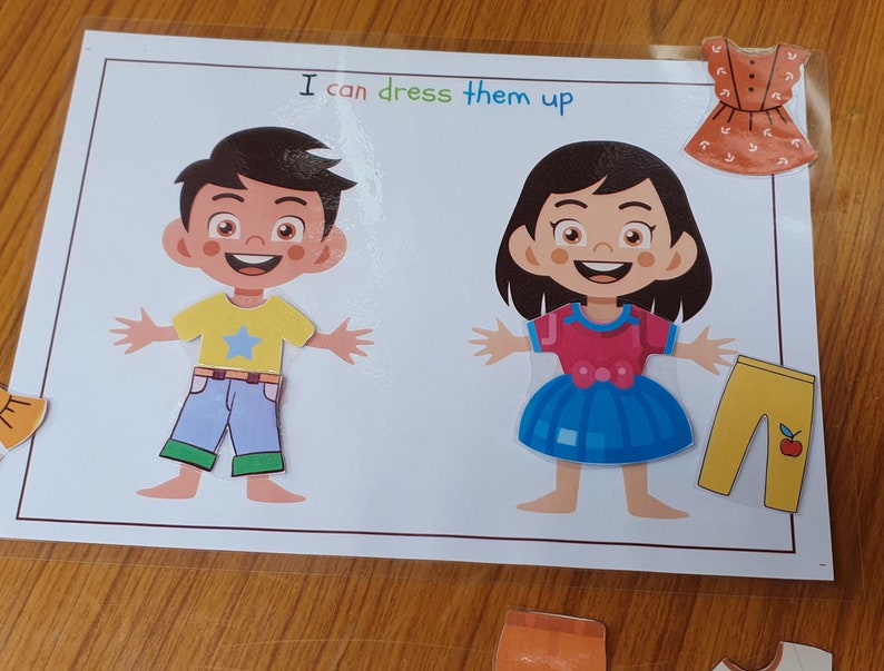 May include: A printable activity sheet with two paper dolls, a boy and a girl, and various clothing items to dress them up. The text on the sheet reads "I can dress them up".