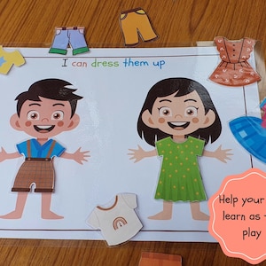 May include: A learning game for children featuring two paper dolls, a boy and a girl, with various clothing items to dress them up. The game includes a blue shirt with a star, a brown and white plaid shirt, a pair of blue jeans, a pair of brown pants, a green dress with white polka dots, a blue dress with a pink bow, a brown dress with white buttons, and a white shirt with a rainbow. The game includes the text "I can dress them up" and "Help your child learn as they play".
