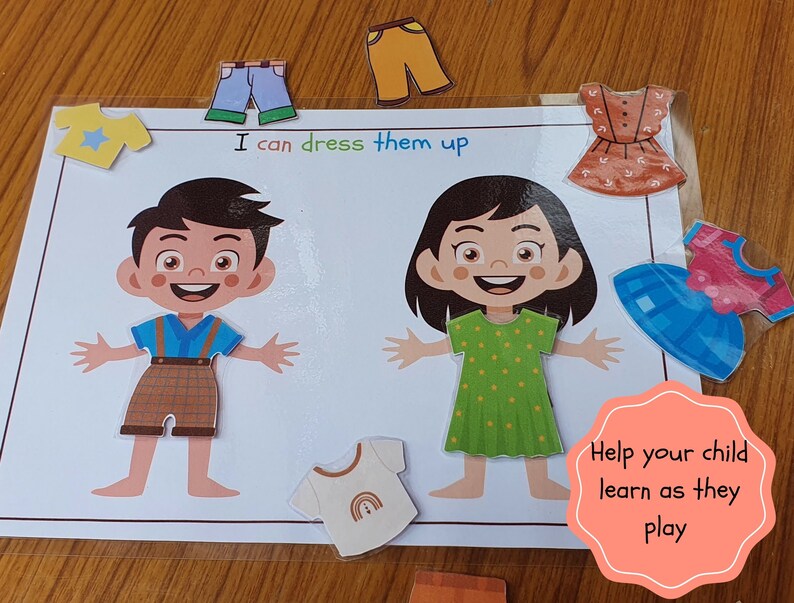 May include: A learning game for children featuring two paper dolls, a boy and a girl, with various clothing items to dress them up. The game includes a blue shirt with a star, a brown and white plaid shirt, a pair of blue jeans, a pair of brown pants, a green dress with white polka dots, a blue dress with a pink bow, a brown dress with white buttons, and a white shirt with a rainbow. The game includes the text "I can dress them up" and "Help your child learn as they play".
