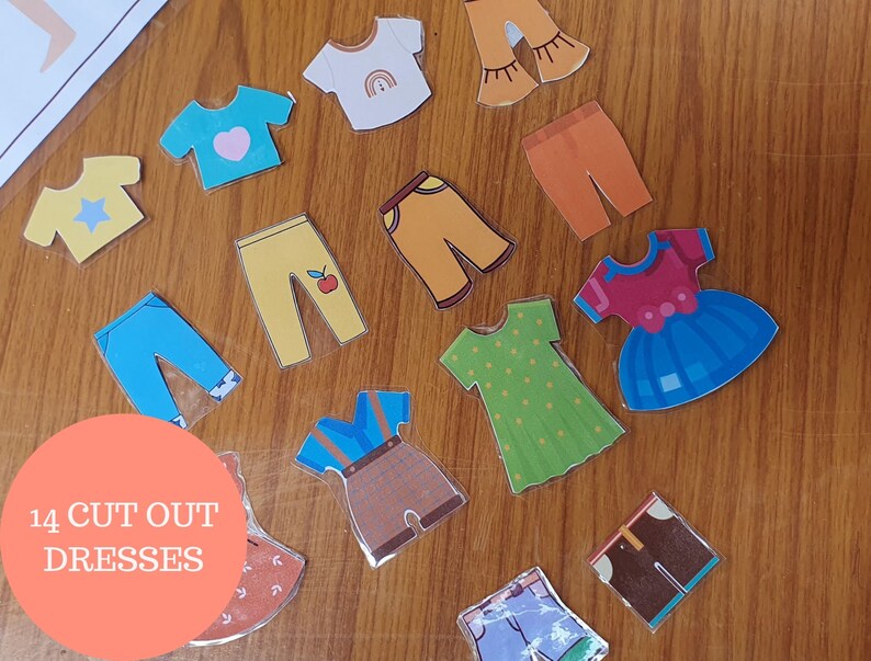 May include: A set of 14 colorful cut-out paper dress shapes, including a blue dress with a red bow, a green dress with white polka dots, and a yellow dress with a red apple. The paper shapes are on a wooden surface.