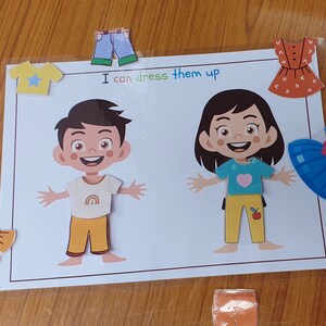 May include: A printable activity for kids featuring two cartoon characters, a boy and a girl, with various clothing items to dress them up. The text on the page reads "I can dress them up".