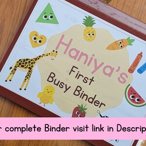 May include: A colorful binder with the text "Haniya's First Busy Binder" and various cartoon images, including a pineapple, a giraffe, a watermelon, a carrot, and crayons.