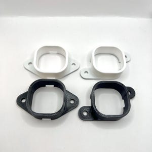 Puede incluir: Cuatro soportes cuadrados impresos en 3D. Dos son blancos y dos son negros. Cada soporte tiene una abertura cuadrada y dos orificios de montaje. Los soportes están diseñados para montarse en una superficie.