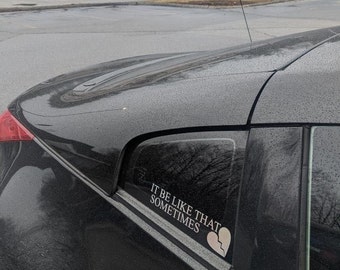May include: A black car with a sticker on the back window that says "It be like that sometimes" with a broken heart graphic.