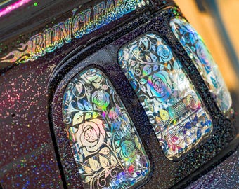 May include: Close-up of a vehicle's window with a floral design. The windows are decorated with iridescent roses and leaves, set against a dark background with glitter. The text "RUN CLEAR" and "clusterfuc." are visible.