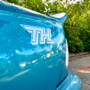 May include: A teal blue car with a white "THL" sticker on the rear.