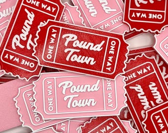 May include: A pile of red and pink paper tickets with the words "Pound Town" printed on them. The tickets are shaped like traditional paper tickets with a scalloped edge and the words "One Way" printed on them.