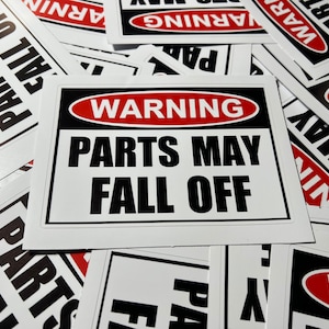 以下が含まれることがあります： 黒と赤の文字で書かれた白い警告サインの束。サインには「警告 部品が落下する可能性があります」と書かれています。