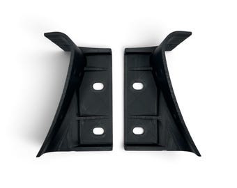 May include: Two identical black L-shaped brackets with curved outer edges. Each bracket features a flat mounting surface with two circular holes for screws, and a perpendicular support arm that extends outward with a slight upward curve.