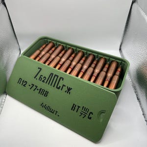 May include: A green ammunition box with a hinged lid, filled with copper-coloured bullets. The box has black text on the front, including "7,62 ЛПС г.х." and "440шт."