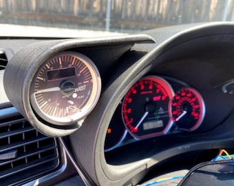 May include: A close-up of a car's dashboard with a boost gauge mounted on the left side. The gauge has a black face with white markings and a red needle. The gauge reads "BOOST" and has a digital display showing the peak boost pressure. The car's dashboard also has two other gauges, one for the speedometer and one for the tachometer.