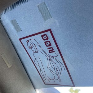 Peut inclure: Un autocollant de fen&ecirc;tre de voiture rouge et blanc avec une image de dessin anim&eacute; d'une femme aux cheveux longs et le mot "Zero Two" dans une bo&icirc;te.