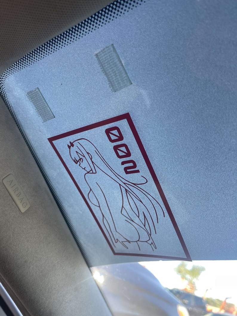 Peut inclure: Un autocollant de fen&ecirc;tre de voiture rouge et blanc avec une image de dessin anim&eacute; d'une femme aux cheveux longs et le mot "Zero Two" dans une bo&icirc;te.