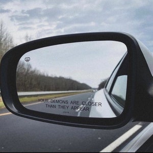Peut inclure: Un r&eacute;troviseur de voiture avec le texte "Your demons are closer than they appear" refl&eacute;t&eacute; dans le verre.