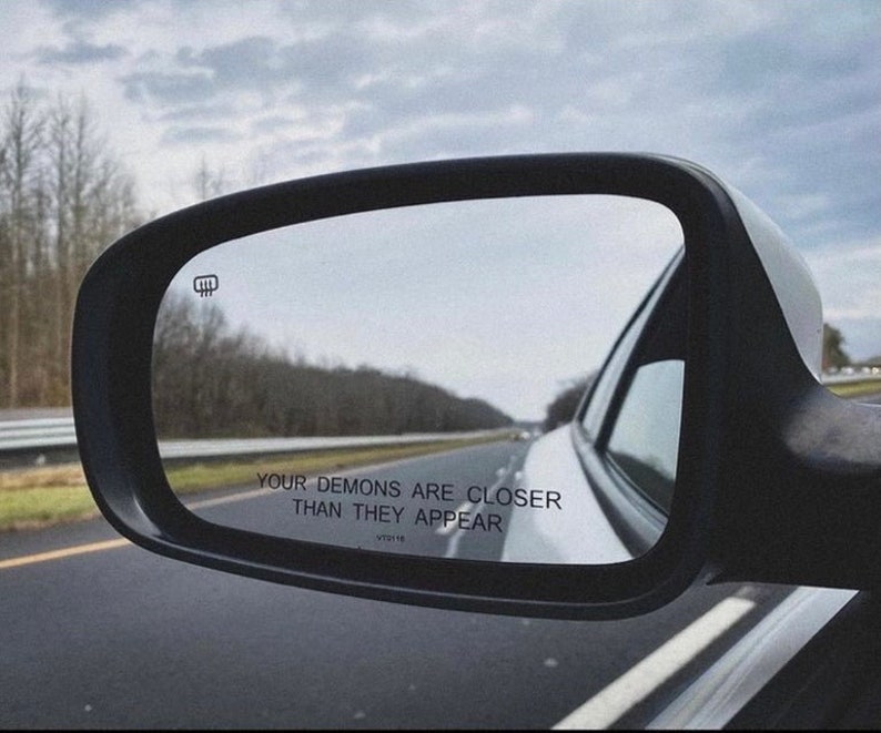 Peut inclure: Un r&eacute;troviseur de voiture avec le texte "Your demons are closer than they appear" refl&eacute;t&eacute; dans le verre.